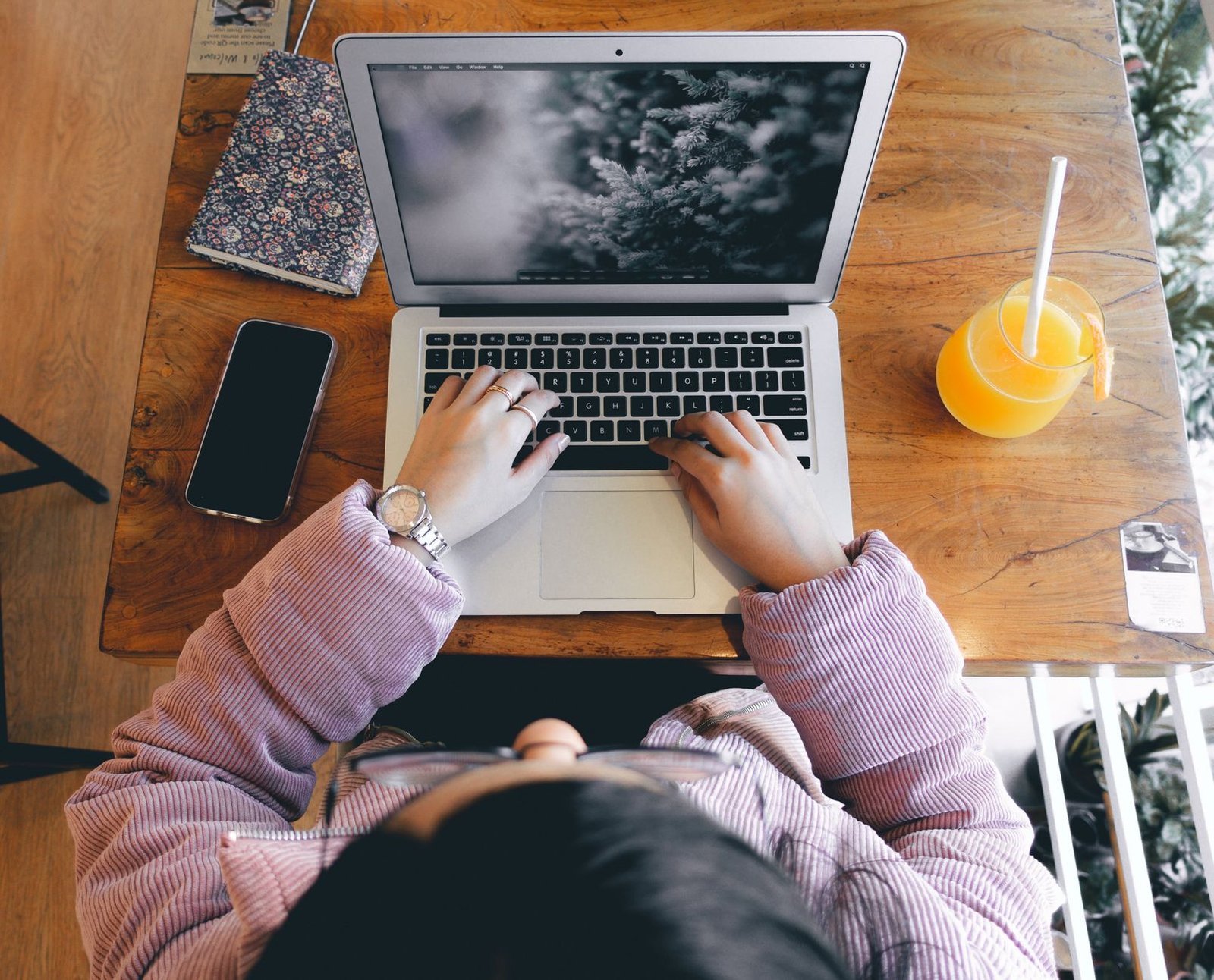 Top view of a person working on a laptop with a smartphone and juice on a wooden desk. — Is Mississippi a Good Place to Live?